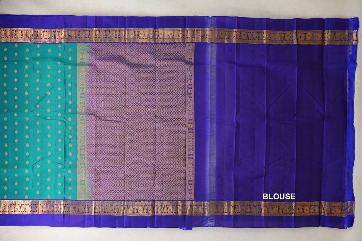 Light weight Kanchipuram silk saree laid flat, showing a peacock green dotted body, deep royal blue gold-patterned borders, a lattice pallu and a blue blouse piece.