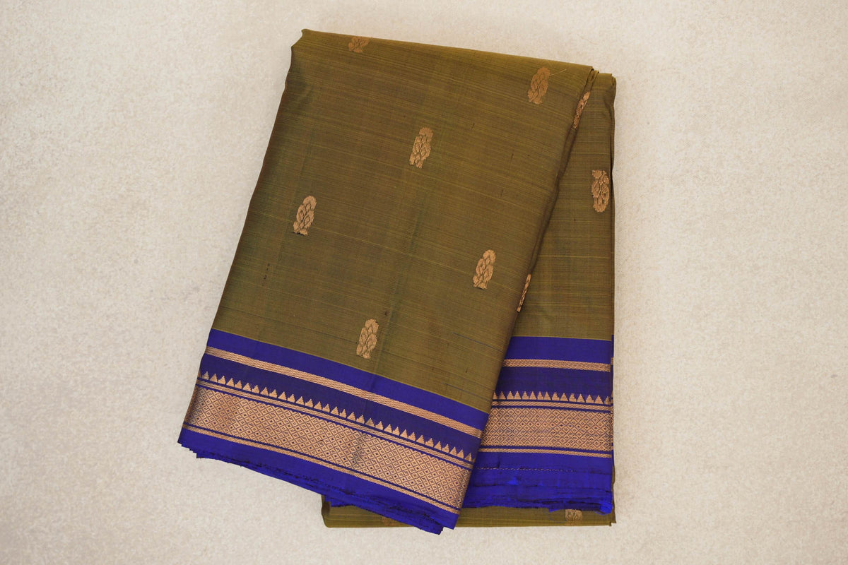 Folded olive green Kanchipuram silk saree with small gold motifs and a deep royal blue border with gold geometric detailing.