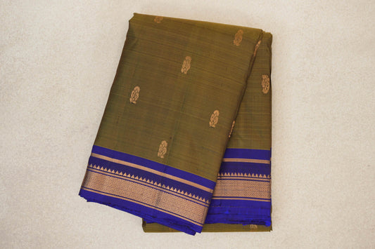 Folded olive green Kanchipuram silk saree with small gold motifs and a deep royal blue border with gold geometric detailing.