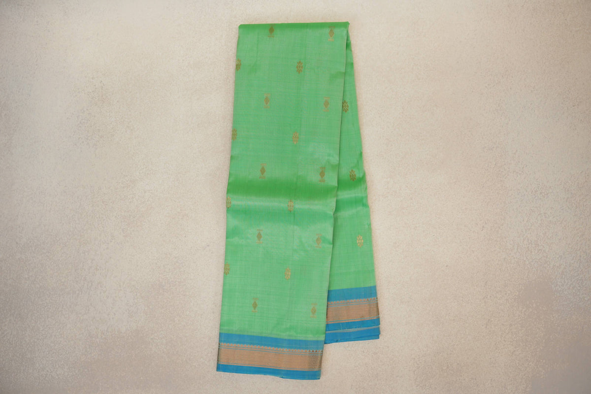 Folded mint green lightweight Kanchipuram silk saree with scattered gold motifs and light turquoise blue borders edged in gold.