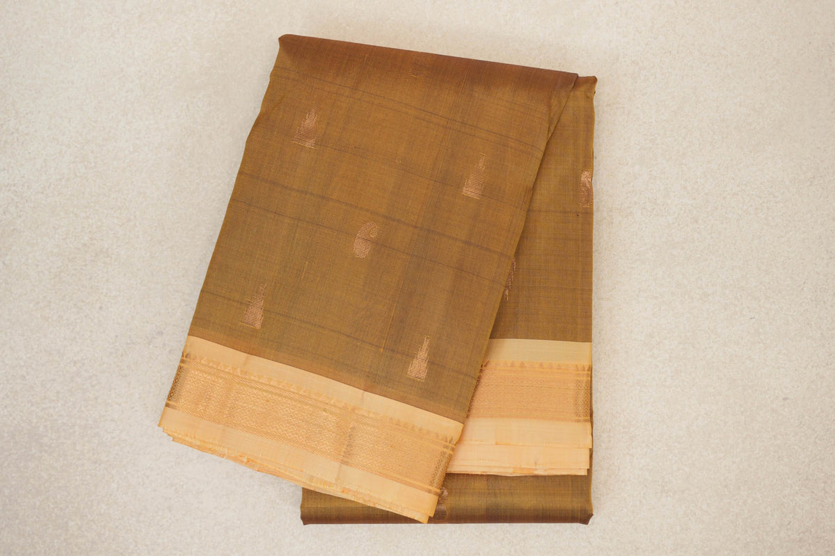 Folded oil mustard Kanchipuram silk saree with small gold accents and sandal borders featuring fine woven patterns.
