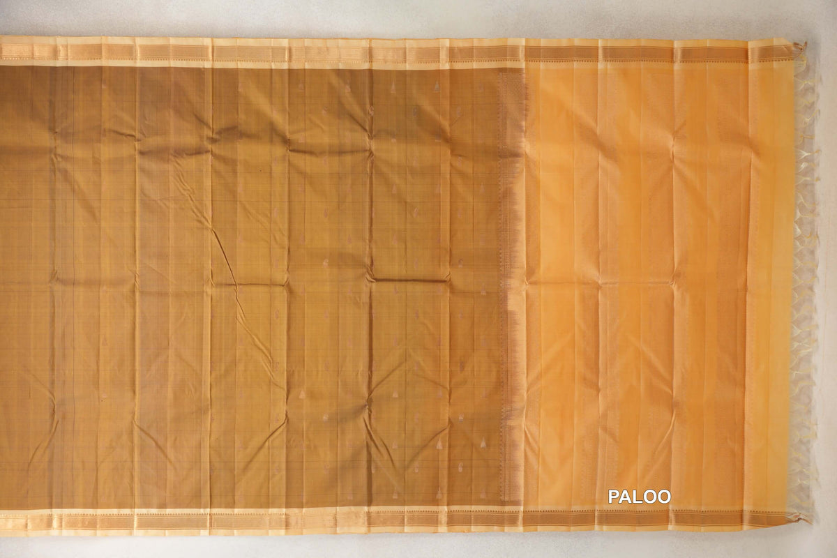 Lightweight Kanchipuram silk saree laid open, showing an oil mustard body with small motifs, sandal borders and a striped sandal pallu with tassels.