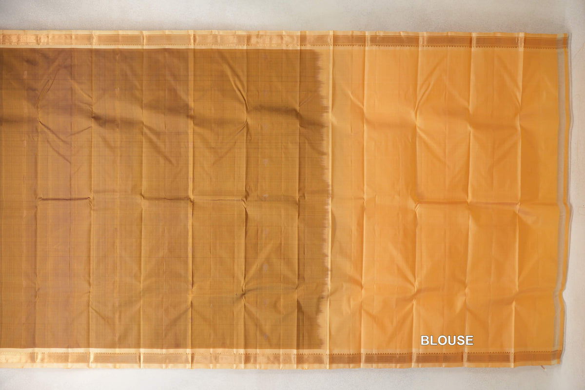 Oil mustard Kanchipuram silk saree laid flat beside its sandal blouse section, with narrow patterned borders along the top and bottom.