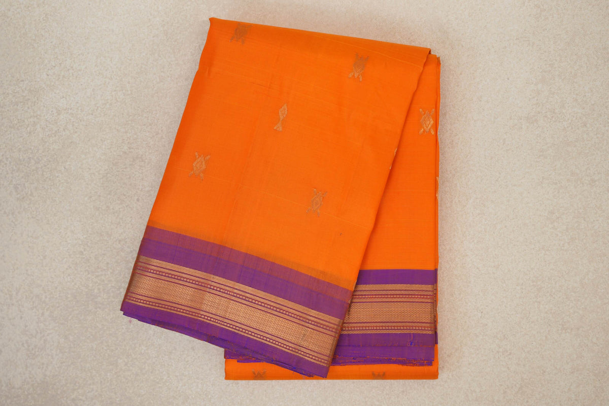 Folded bright orange Kanchipuram silk saree with small gold motifs and a violet border patterned with gold stripes.