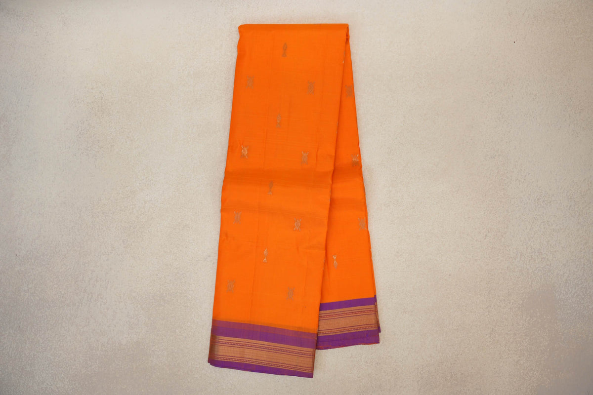 Folded bright orange Kanchipuram silk saree with scattered small gold motifs and violet borders woven with gold stripes.