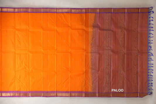 Bright orange Kanchipuram silk saree spread flat, with small scattered motifs, violet-edged gold borders and a floral pallu with violet tassels.