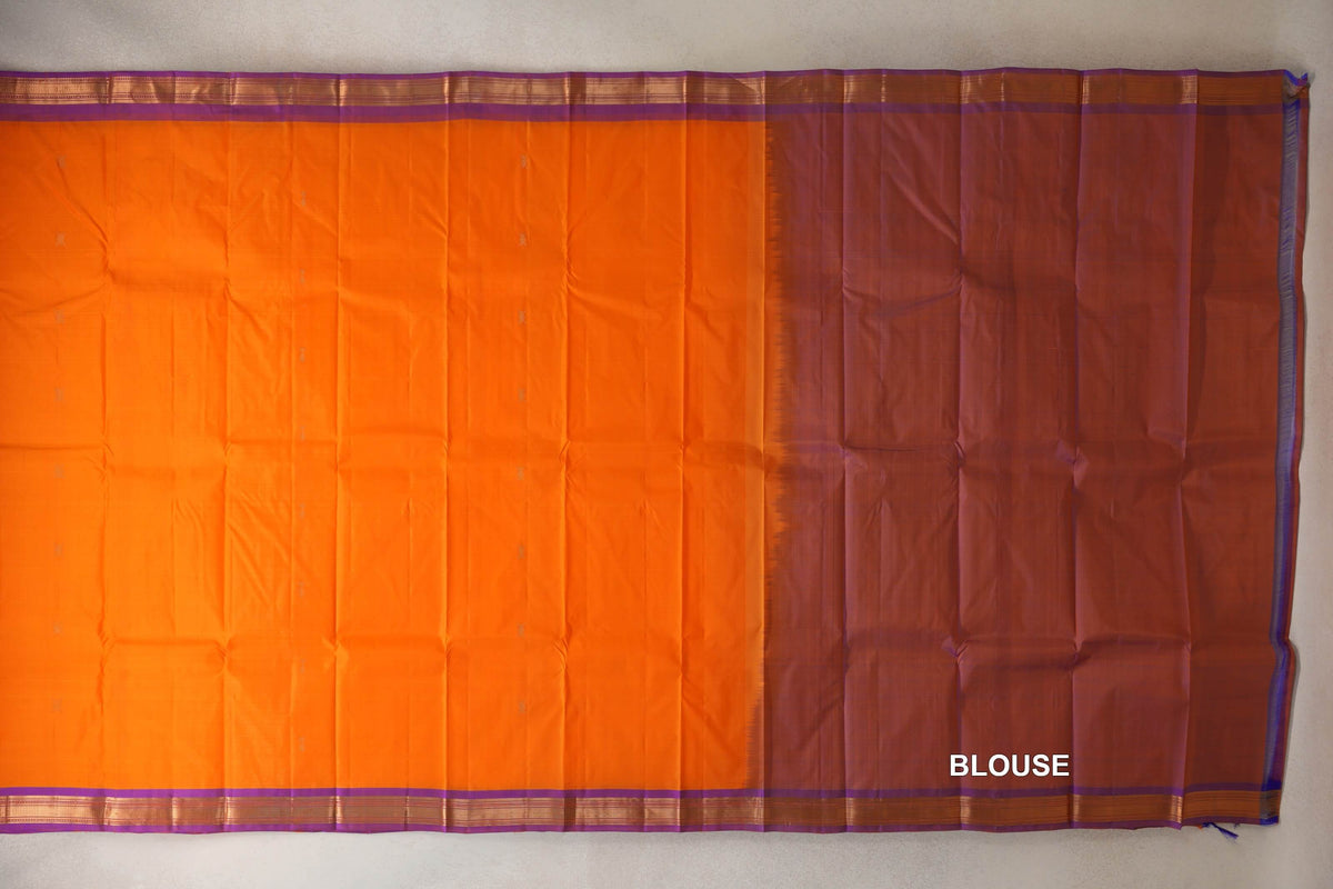 Bright orange Kanchipuram silk saree laid flat, with small scattered motifs, violet and gold-striped borders, and a purple blouse section at right.