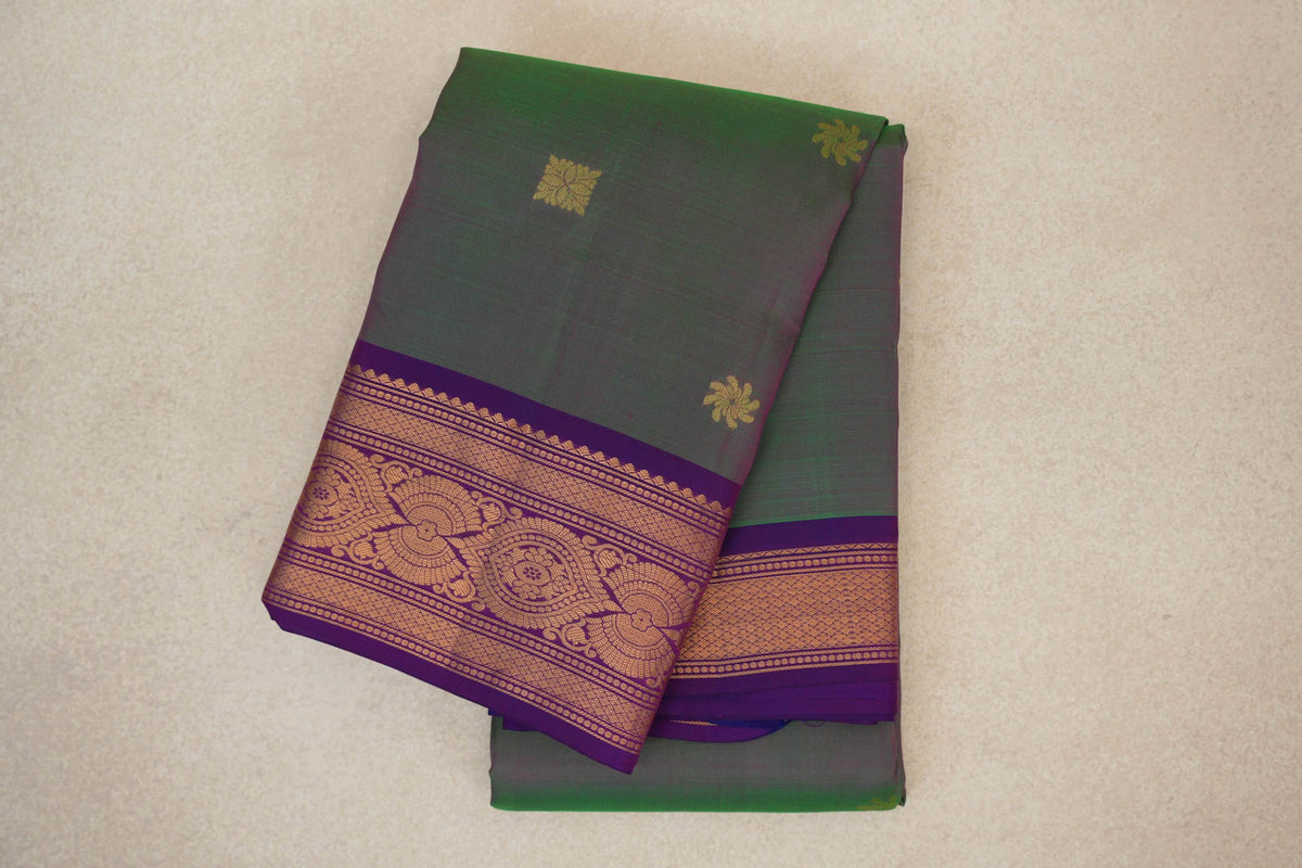 Folded lightweight Kanchipuram silk saree with a green and pink body, small gold motifs, and an ornate gold-patterned violet purple border.