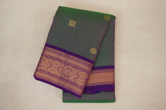 Folded lightweight Kanchipuram silk saree with a green and pink body, small gold motifs, and an ornate gold-patterned violet purple border.