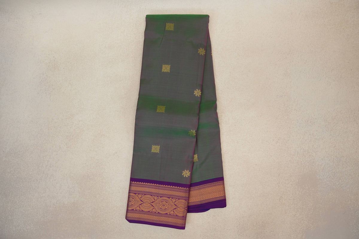 Folded lightweight Kanchipuram silk saree with a muted green and pink body, scattered gold motifs, and a violet purple border with gold patterns.