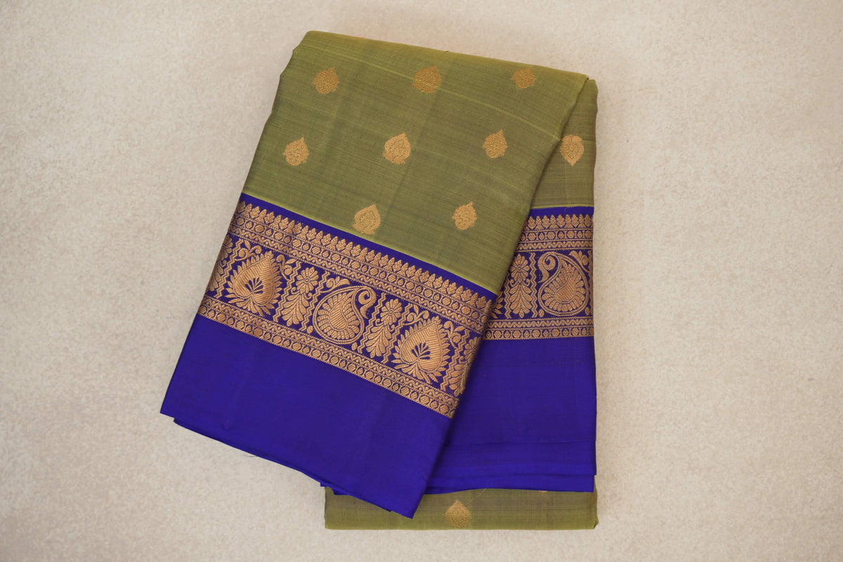 Folded olive green Kanchipuram silk saree with scattered gold motifs and a royal purple border featuring gold paisley and floral designs.