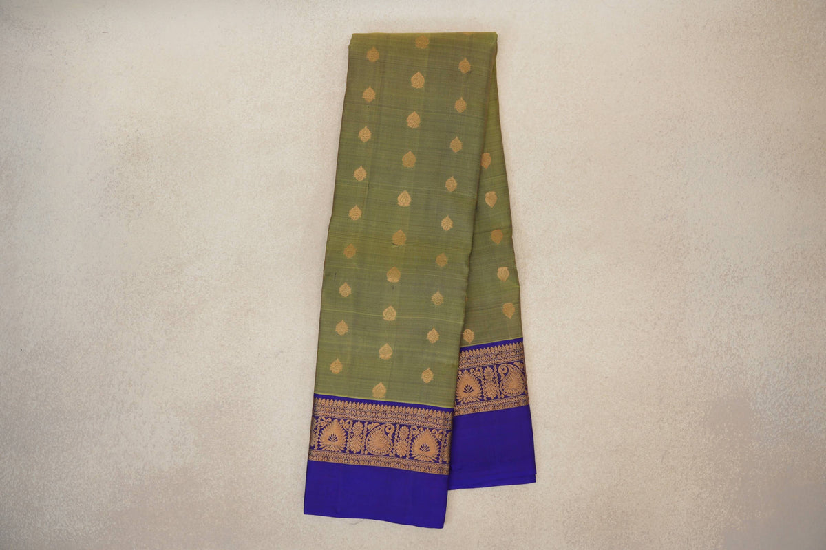 Folded olive green Kanchipuram silk saree with scattered gold motifs and royal purple borders woven with gold paisley and floral designs.