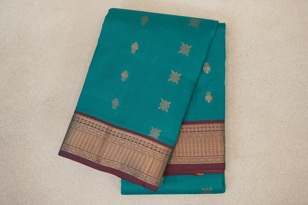 Folded peacock green Kanchipuram silk saree with scattered gold motifs and a wide gold-patterned border edged in maroon.