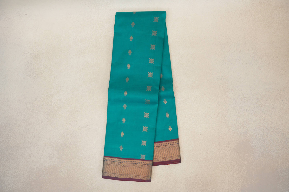 Folded peacock green Kanchipuram silk saree with scattered gold motifs and a patterned gold border edged in maroon.