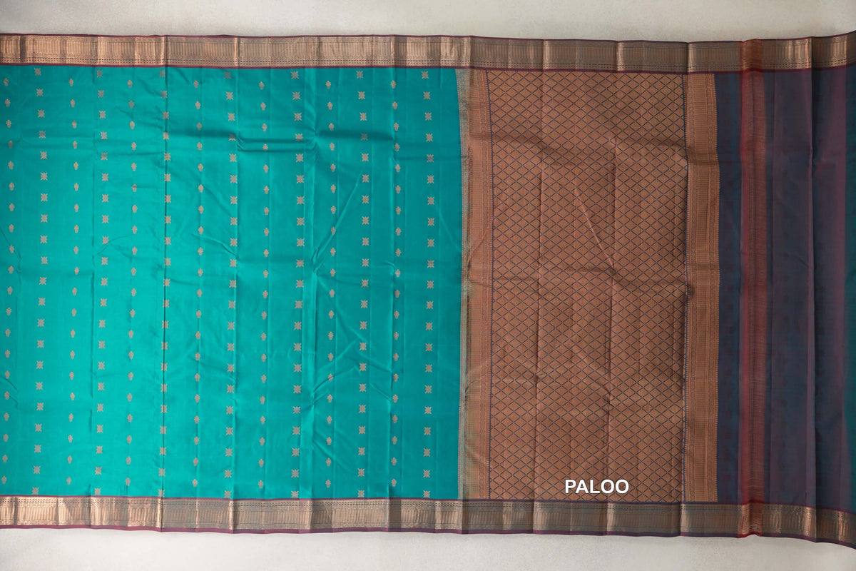 Lightweight Kanchipuram silk saree spread out, with a peacock green body, small gold motifs, ornate borders and a geometric-patterned pallu.