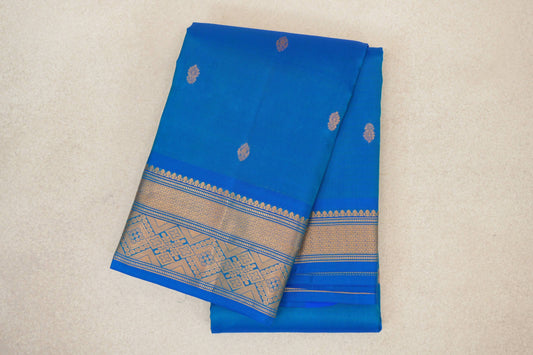 Folded peacock blue lightweight Kanchipuram silk saree with scattered gold motifs and a broad geometric floral border.