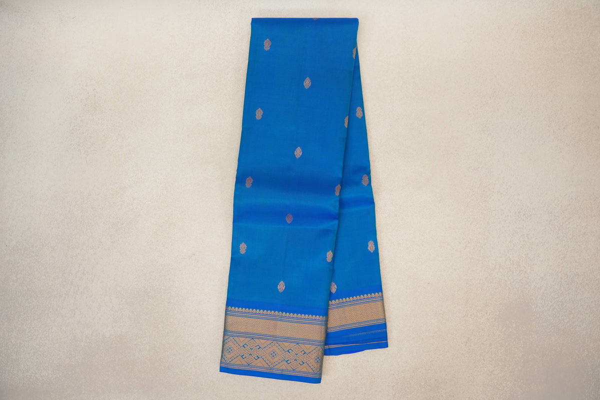 Peacock blue lightweight Kanchipuram silk saree folded lengthwise, with scattered gold motifs and patterned gold borders visible at the ends.