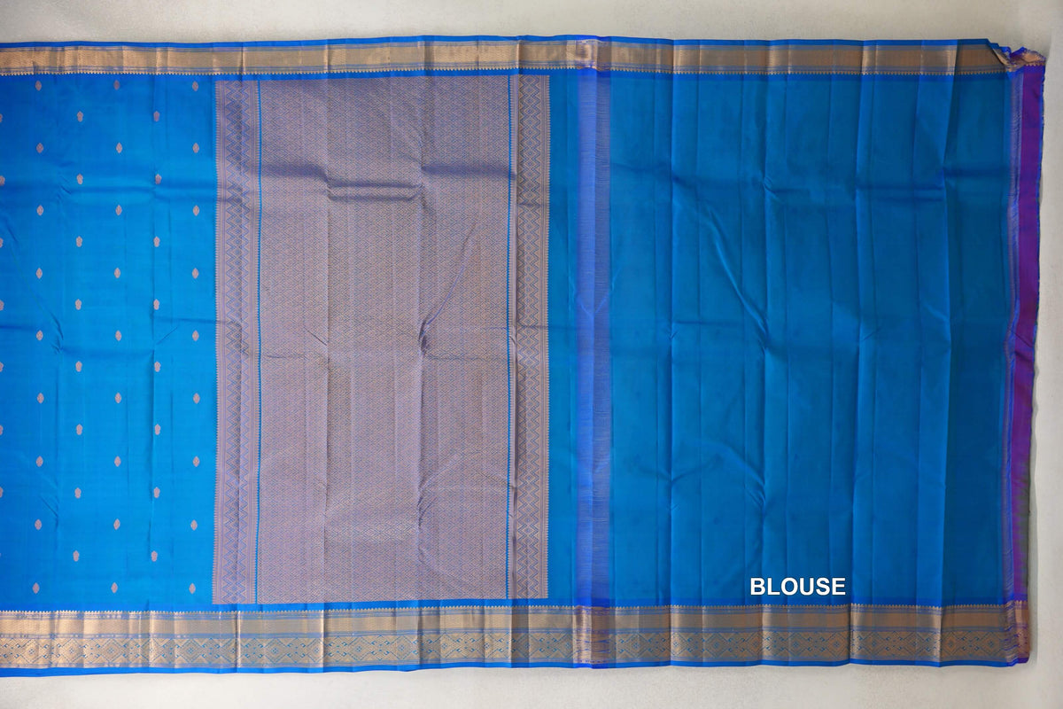 Peacock blue Kanchipuram silk saree spread out, showing a small-motif body, patterned gold-toned pallu and borders, and a plain blue blouse piece.