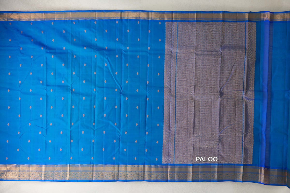 Peacock blue lightweight Kanchipuram silk saree spread out, with small gold-toned motifs, patterned borders and a geometric pallu.