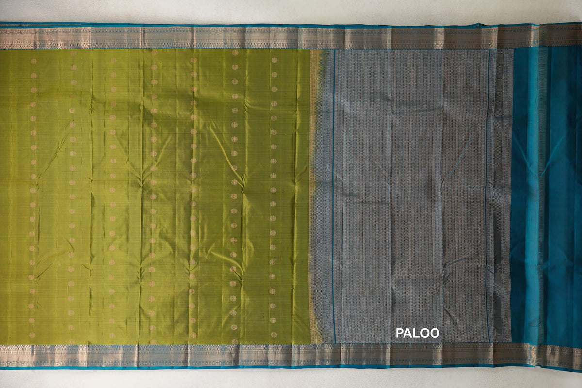 Olive Green Kanchipuram silk saree spread flat, with rows of small gold dots, teal blue woven borders and a densely patterned pallu.