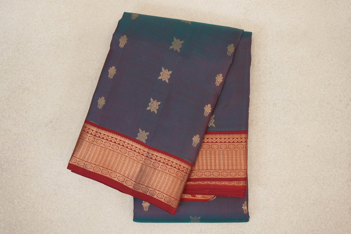 Folded lightweight Kanchipuram silk saree with a teal blue and red body, scattered gold motifs and a deep red border with gold geometric patterns.