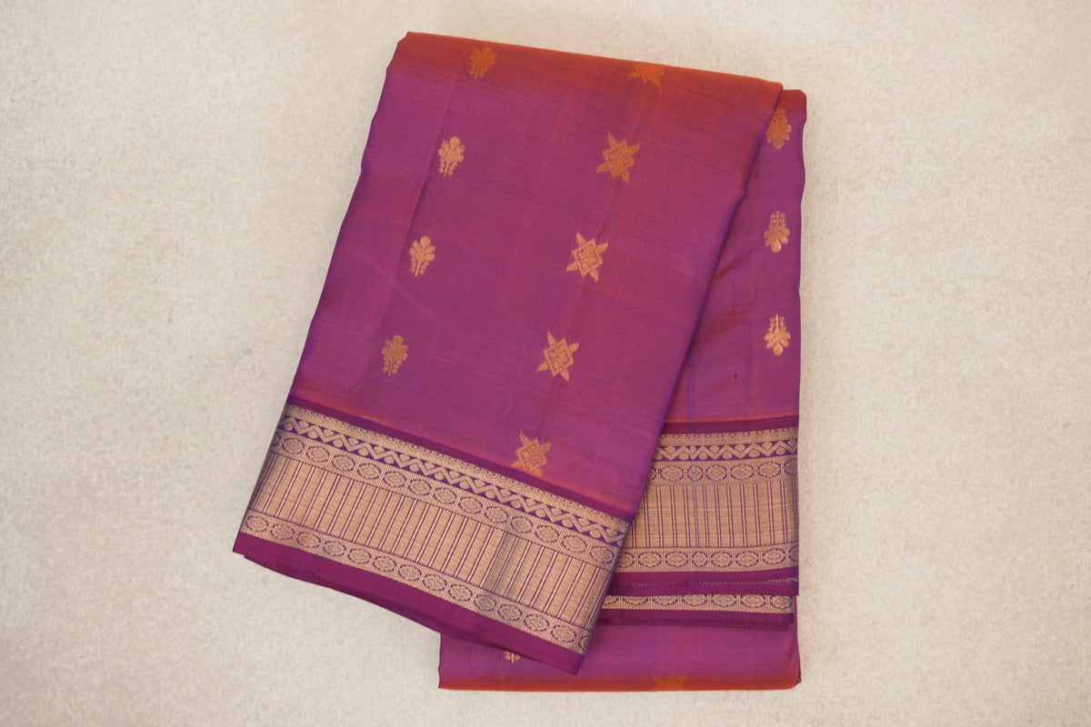 Folded blue and red light weight Kanchipuram silk saree with scattered gold motifs and a wide patterned gold zari border.