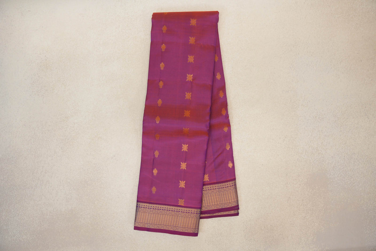 Folded lightweight Kanchipuram silk saree in blue and red, appearing purple, with scattered gold motifs and broad patterned gold borders.