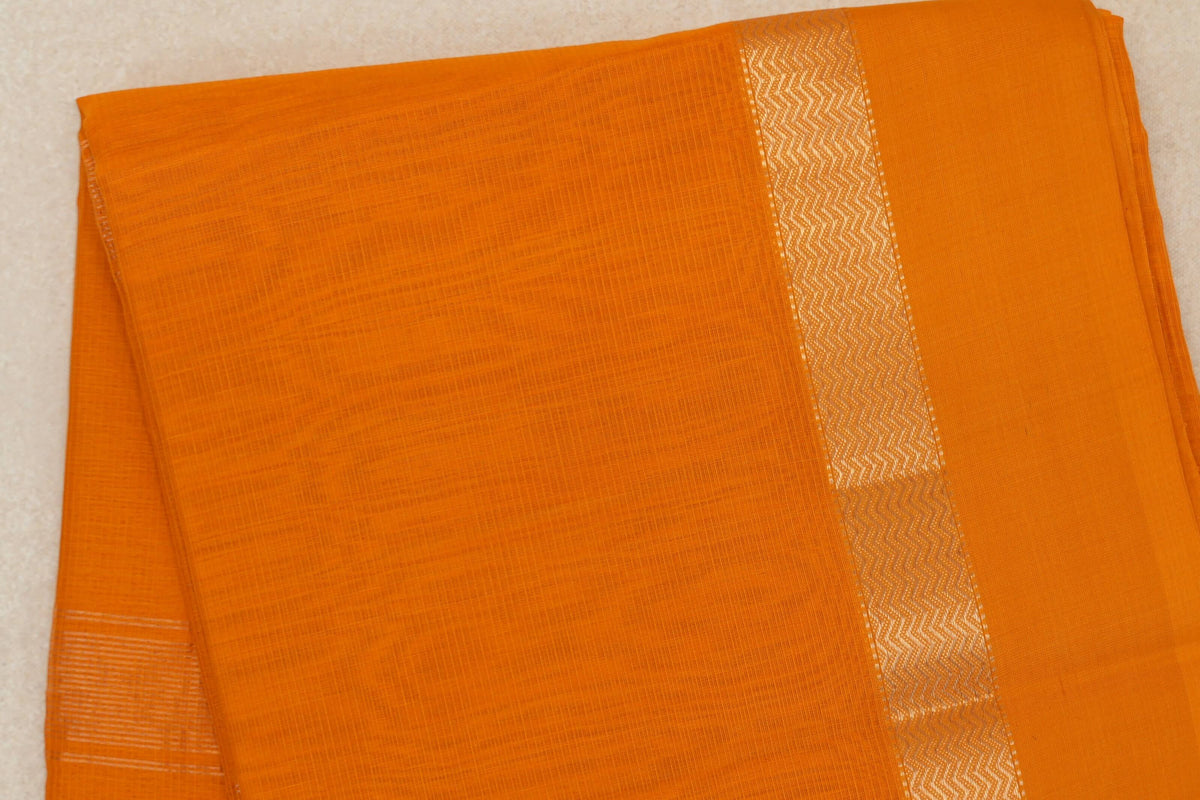 Folded mango yellow Maheshwari silk-cotton saree with a fine woven grid and a shimmering zigzag border.