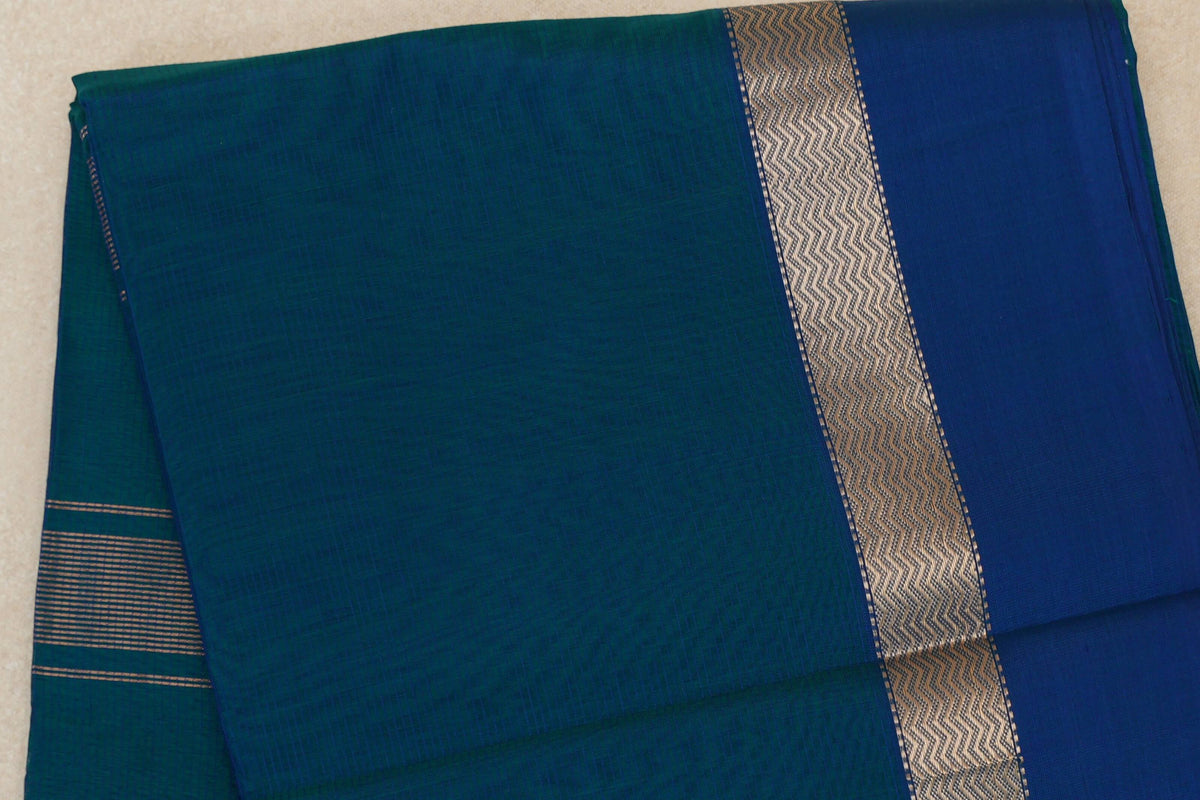 Folded Peacock Blue Maheshwari silk cotton saree showing a subtly textured body, metallic zigzag band and deep Peacock Blue border.