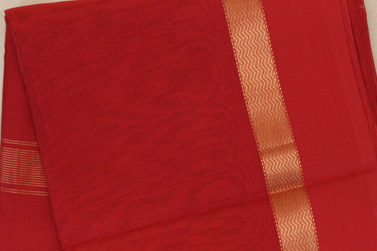 Folded vermilion red Maheshwari silk cotton saree showing a fine checked body, a gold zigzag border and narrow gold stripes at one edge.