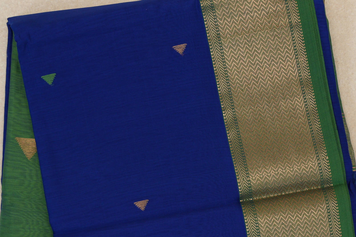 Folded royal blue Maheshwari silk-cotton saree with small triangular motifs and a broad leaf green border with gold-colored zigzags.