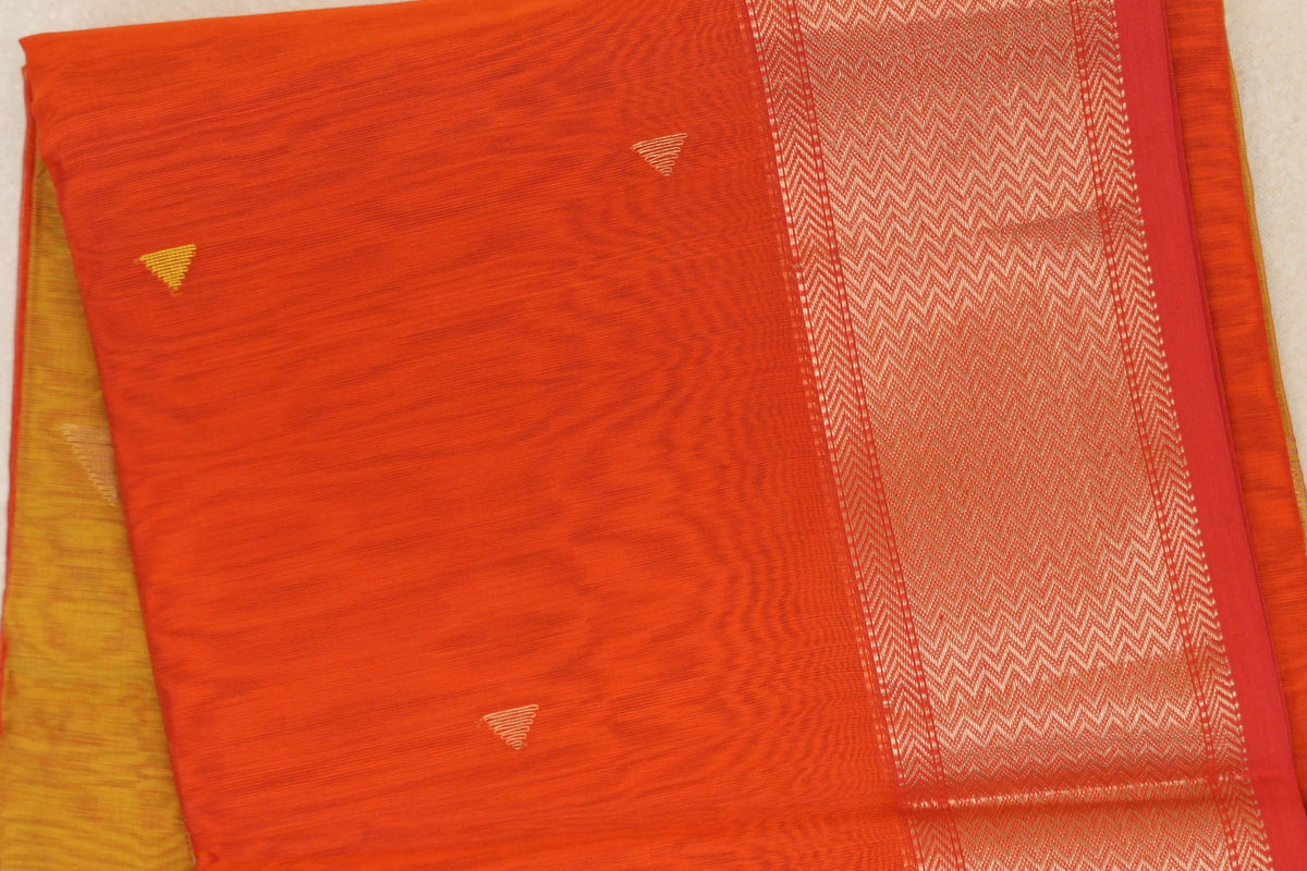 Folded Maheshwari silk cotton saree with a reddish orange body, small gold-toned triangles and a wide orangish red border with chevron pattern.