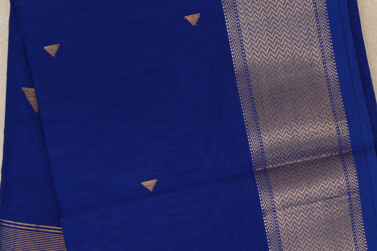 Close-up of a deep royal blue Maheshwari silk cotton saree with small gold-toned triangular motifs and a wide chevron-patterned border.