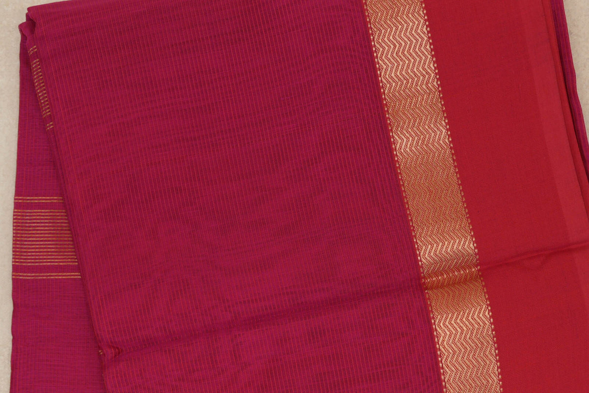 Folded Maheshwari silk cotton saree showing a bright rani pink body, deep rani pink border and a gold-toned zigzag band.