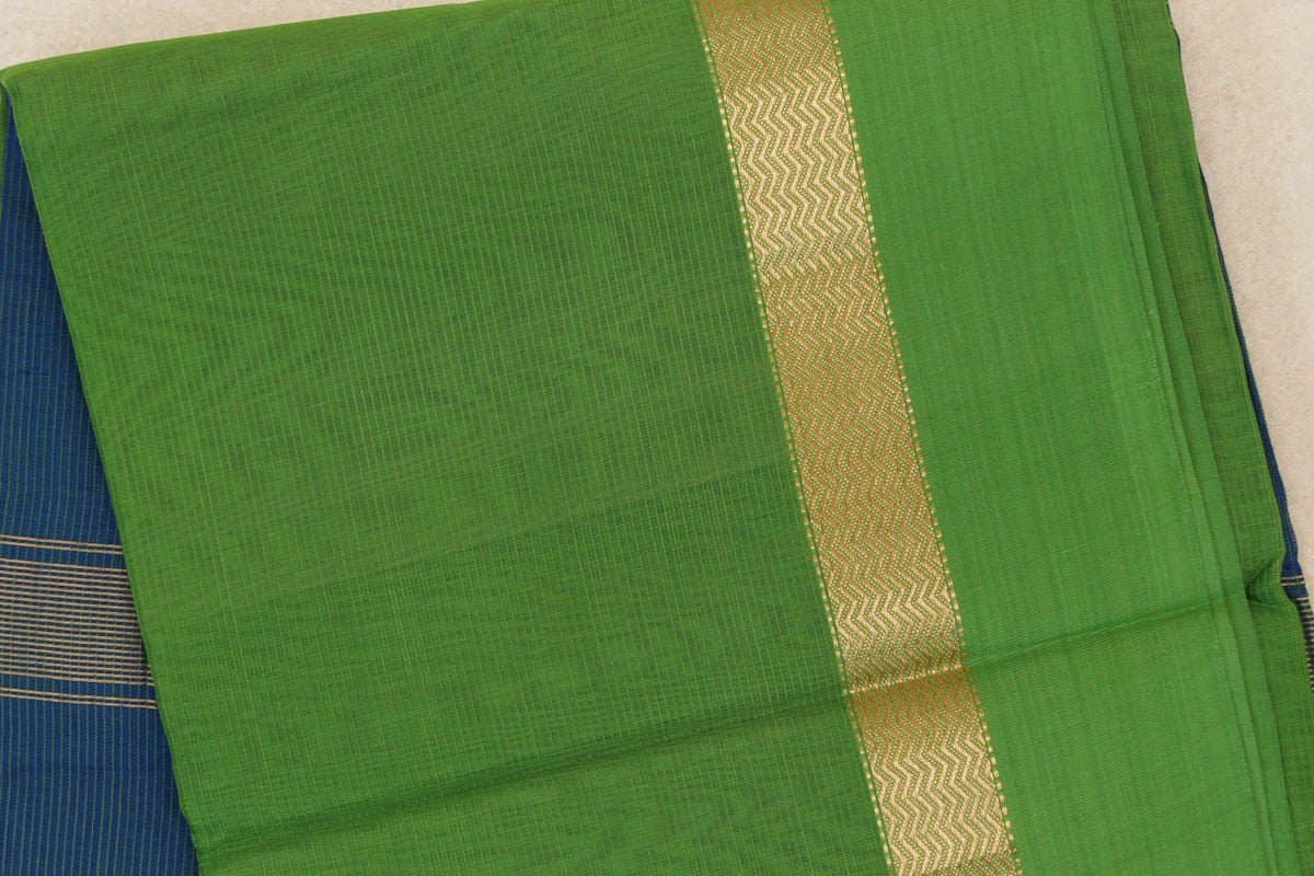 Folded bright leaf green Maheshwari silk cotton saree with a gold wavy-patterned stripe and a glimpse of peacock blue fabric at the side.