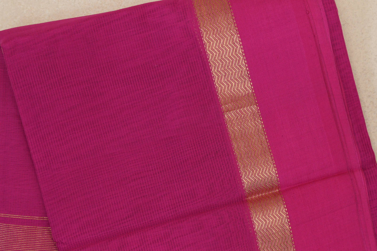 Folded bright rani pink Maheshwari silk cotton saree showing a fine grid texture and a pink border with a gold wavy band.
