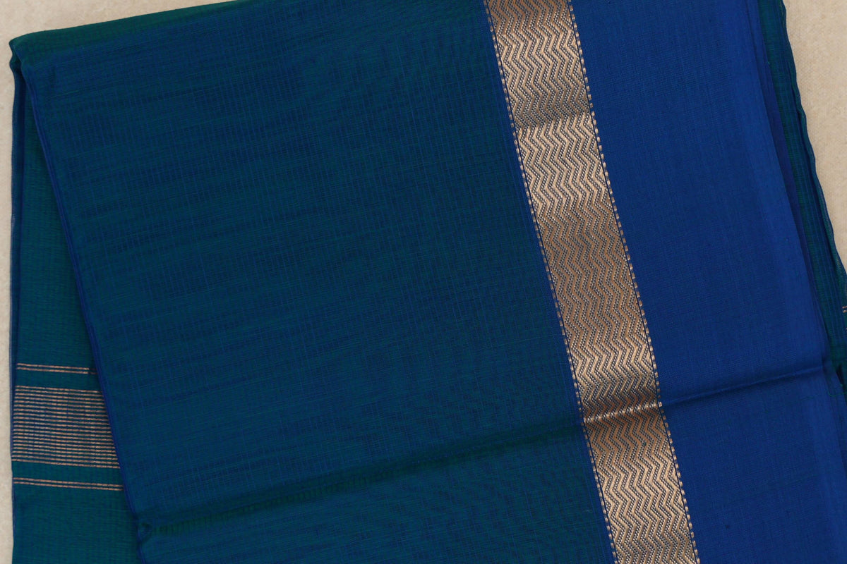 Folded Peacock Blue Maheshwari silk cotton saree with a Deep Peacock Blue border, a metallic zigzag band and fine stripes at one end.