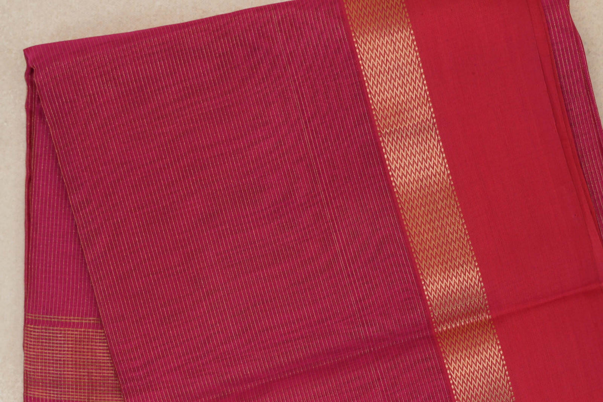 Folded Rani Pink Maheshwari silk cotton saree with fine gold stripes, a zigzag-patterned gold border and a plain pink panel.