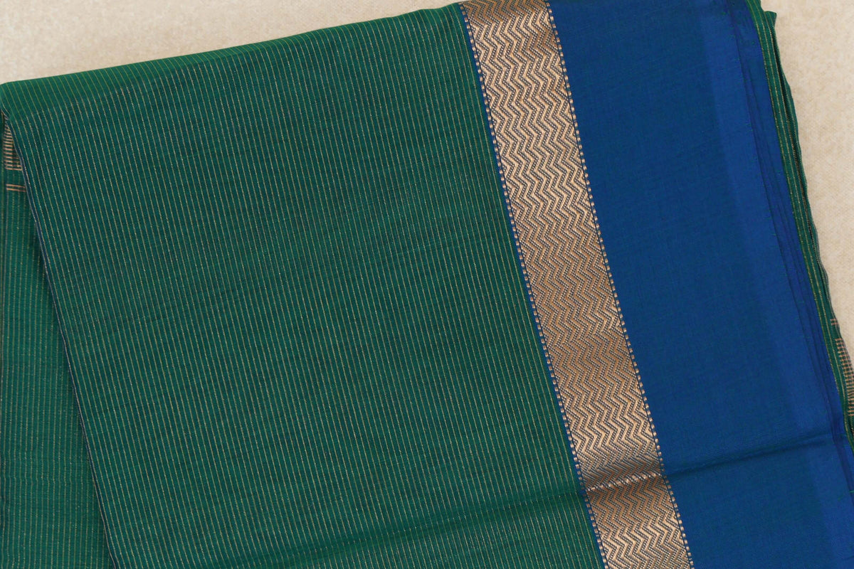 Folded Maheshwari silk-cotton saree showing a bottle green body with fine gold stripes and a peacock blue border with a gold zigzag band.