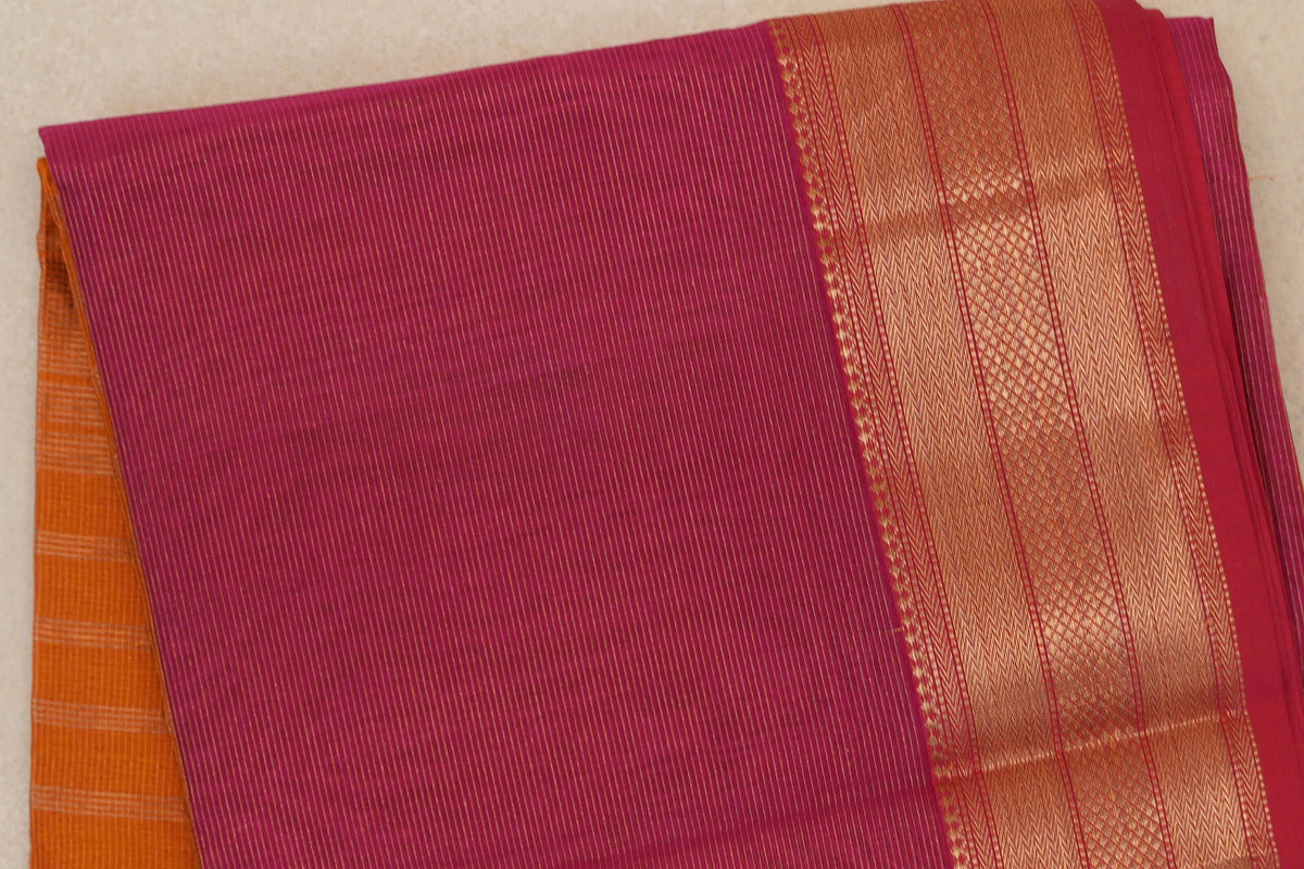 Folded rani pink Maheshwari silk cotton saree with fine gold stripes, a broad woven border and orange fabric peeking out beneath.