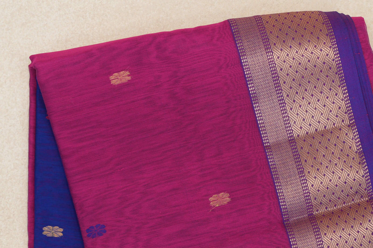 Close-up of a folded rani pink Maheshwari silk cotton saree with small gold motifs, a royal purple and gold geometric border, and royal blue fabric peeking out.