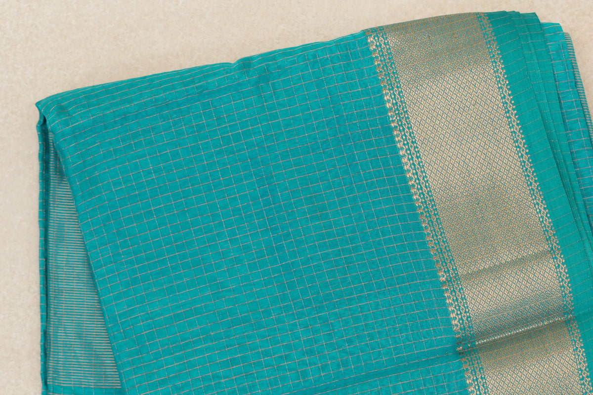 Folded turquoise green Maheshwari silk-cotton saree with a fine checked body and a broad gold-toned woven border.