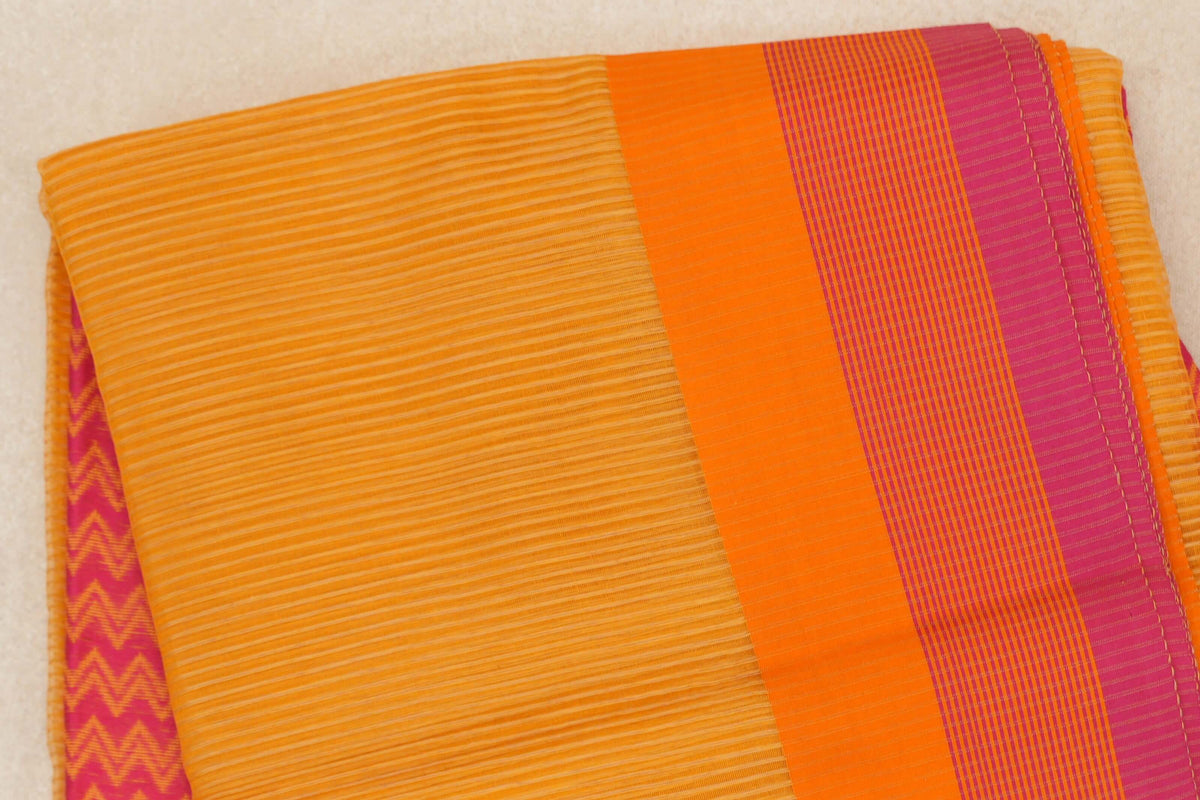 Folded Maheshwari silk cotton saree with a finely striped mango yellow body, orange and rani pink border, and a glimpse of pink zigzag fabric beneath.