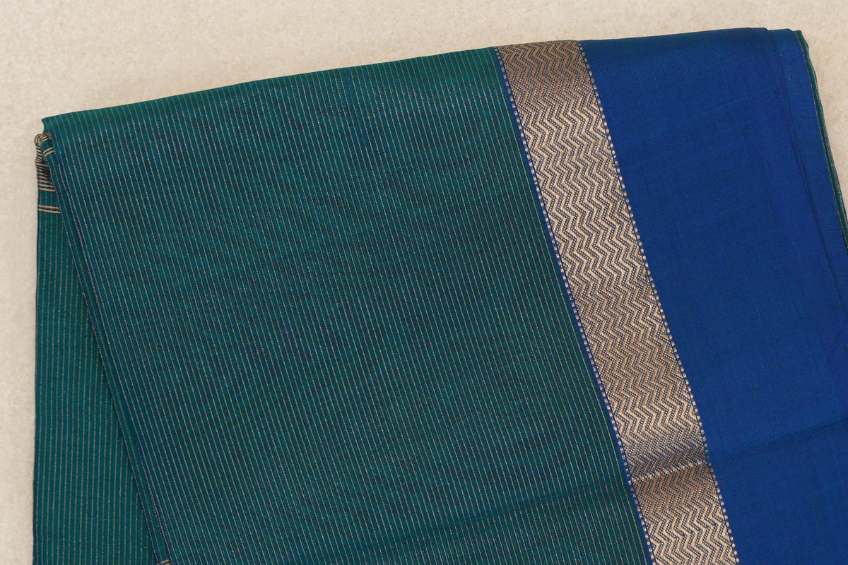 Folded Maheshwari silk cotton saree showing a teal green body with fine metallic stripes and a royal blue border with a zigzag-patterned band.