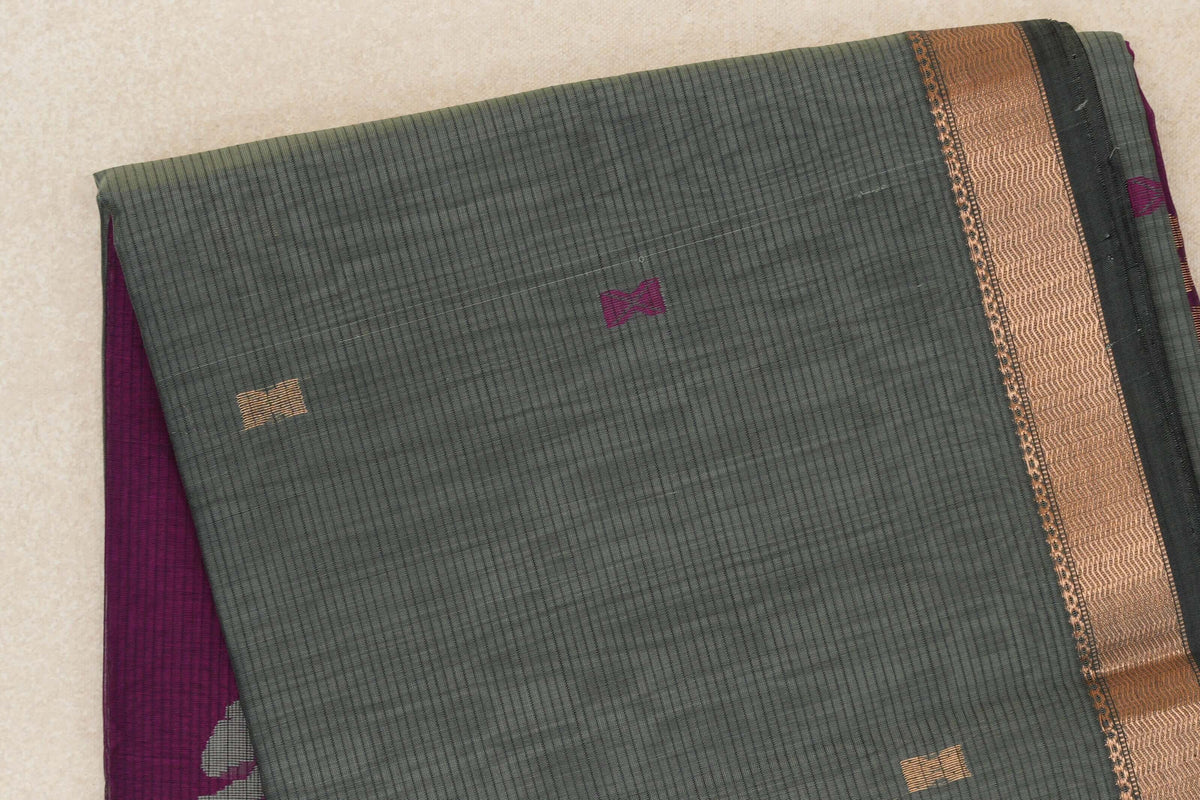 Folded sage green Maheshwari silk cotton saree with fine checks, small magenta and gold accents, a copper-gold border band, and deep magenta fabric peeking out.