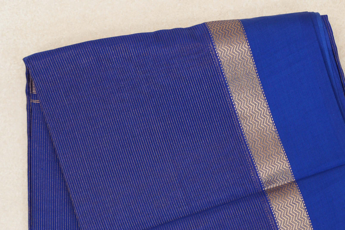 Folded deep royal blue Maheshwari silk-cotton saree with fine gold stripes, a zigzag-patterned band and a plain blue section.
