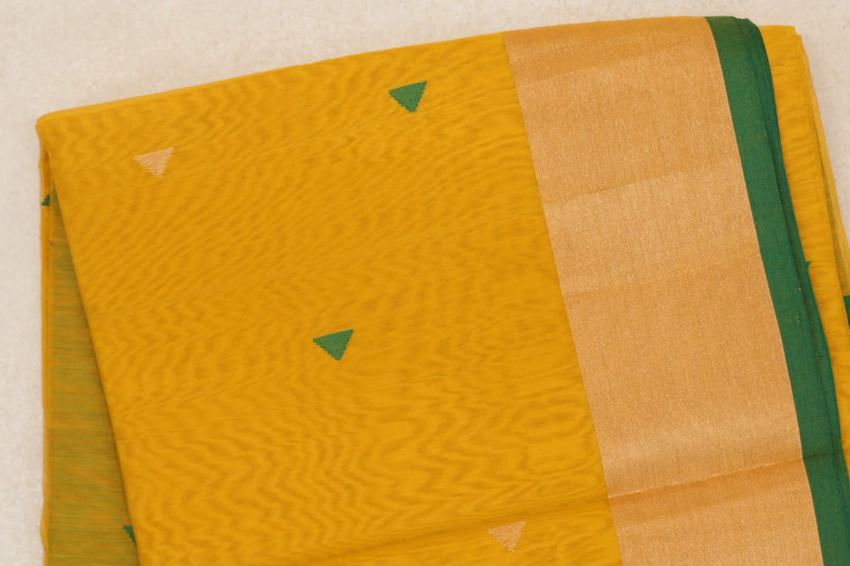 Folded turmeric yellow Maheshwari silk-cotton saree with scattered green and pale gold triangles, a broad pale gold border and bottle green edge.