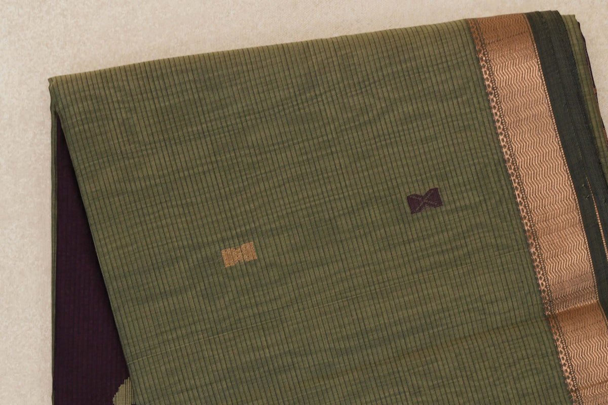 Folded muted olive green Maheshwari silk cotton saree with fine stripes, small gold and plum motifs, a patterned copper-toned border and plum fabric peeking beneath.