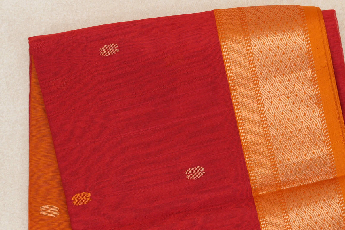 Folded Maheshwari silk cotton saree showing a tomato red body with small striped motifs and a mustard orange geometric border with red selvedge.