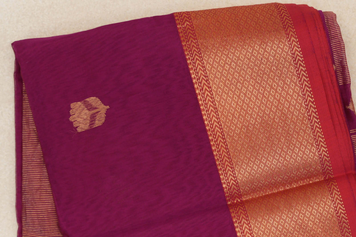 Folded reddish magenta Maheshwari silk cotton saree with a small gold motif and a broad patterned gold border edged in pinkish red.